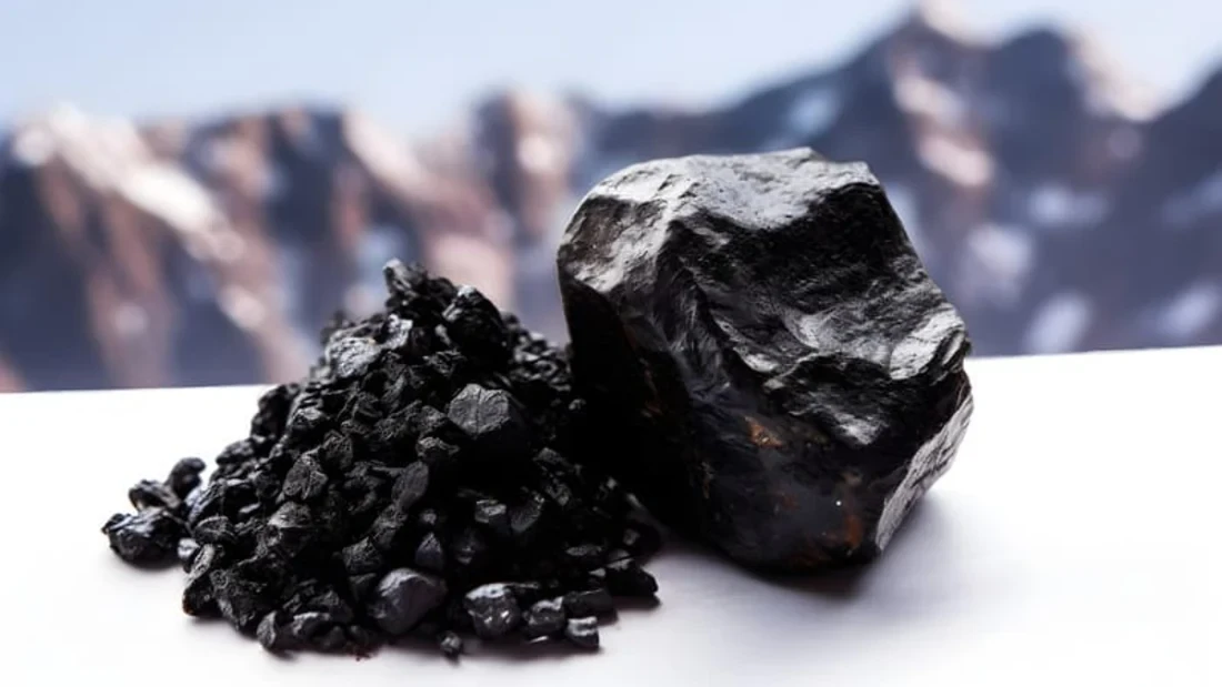 A close-up of raw Shilajit resin and crushed pieces on a white surface with blurred mountain peaks in the background, showcasing its natural and mineral-rich origin.